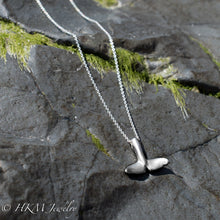Load image into Gallery viewer, underside of whale tail necklace in sterling silver by hkm jewelry on a jetty rock with algae
