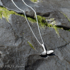 underside of whale tail necklace in sterling silver by hkm jewelry on a jetty rock with algae