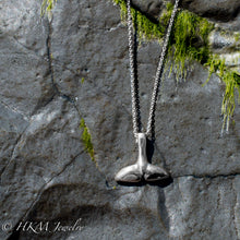 Load image into Gallery viewer, top side of silver dolphin tail necklace by hkm jewelry on a jetty rock with alage
