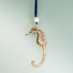 cast bronze seahorse ornament with freshwater pearl and navy blue satin ribbon by hkm jewelry