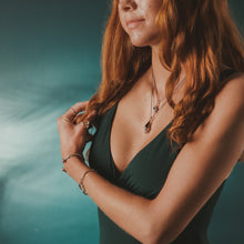 Load image into Gallery viewer, Woman with red hair wearing a green top against a blurred natural background
