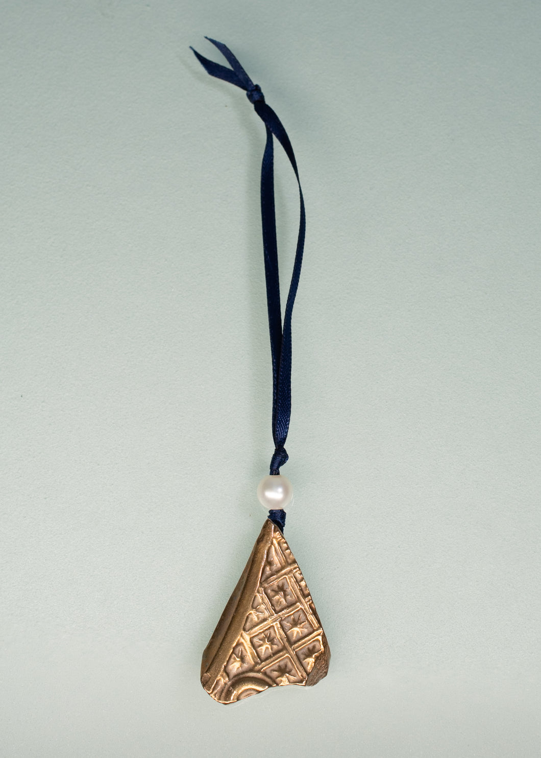 Bronze triangle-shaped ornament with a pearl and blue ribbon on a light gray background