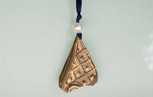 Load image into Gallery viewer, Bronze ornament with embossed design on a blue ribbon against a light gray background

