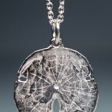Load image into Gallery viewer, backside of small silver sand dollar shell necklace on cable chain with blue gradient background
