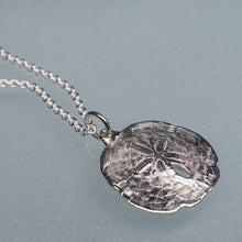 Load image into Gallery viewer, small silver sand dollar shell necklace on cable chain on light blue background
