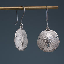 Load image into Gallery viewer, silver sand dollar earrings on brass earring display with dark blue grey background
