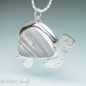 side view of hand sawn and pierced sterling silver sea turtle necklace with fossilized clam shell shard bezel setting
