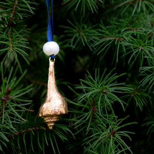 cast bronze lightning whelk ornament from key west florida with freshwater pearl and navy blue satin ribbon by hkm jewelry on evergreen tree