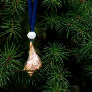 back view of cast bronze lightning whelk ornament from key west florida with freshwater pearl and navy blue satin ribbon by hkm jewelry on evergreen tree