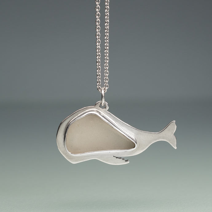 white sea glass whale necklace in silver on blue green background
