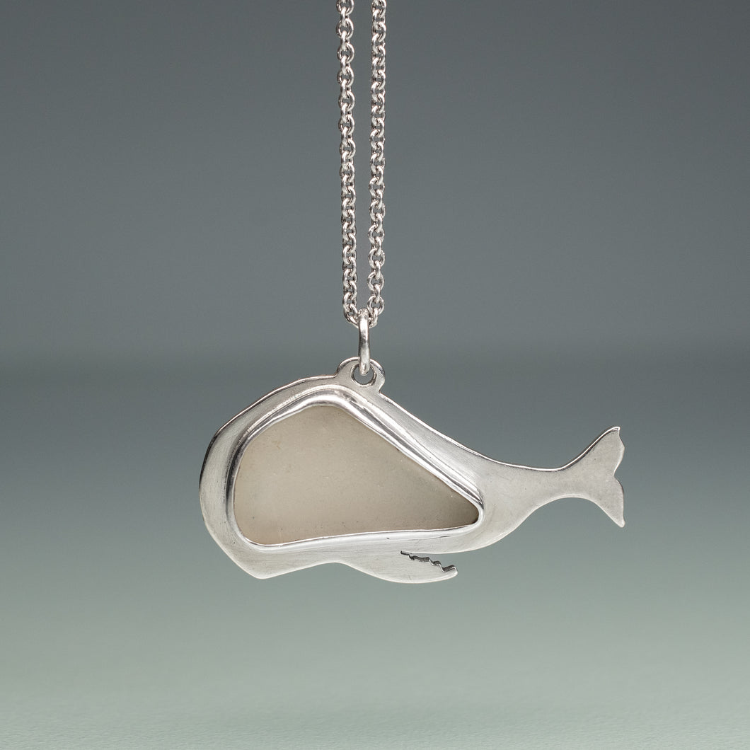 white sea glass whale necklace in silver on blue green background
