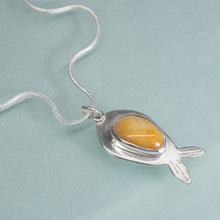 Load image into Gallery viewer, Silver pendant with a yellow stone on a light blue background
