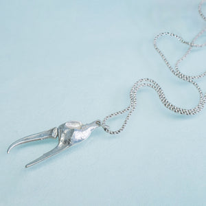 underside view of the cast fiddler crab claw necklace in recycled silver laying on a blue background by hkm jewelry