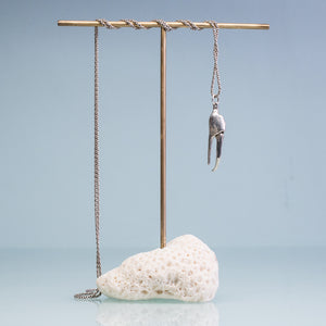 underside view of the cast fiddler crab claw necklace in recycled silver hanging from brass and coral necklace display on a blue background by hkm jewelry