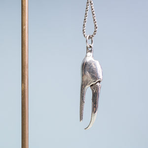 close up view of the cast fiddler crab claw necklace in recycled silver hanging from brass and coral necklace display on a blue background by hkm jewelry