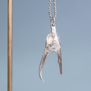underside view of the open pincer of the cast fiddler crab claw necklace in recycled silver hanging from brass and coral necklace display on a blue background by hkm jewelry