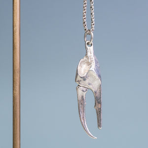 underside view and close up of the cast fiddler crab claw necklace in recycled silver hanging from brass and coral necklace display on a blue background by hkm jewelry