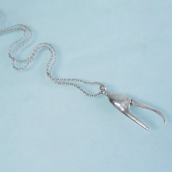 cast fiddler crab claw in recycled silver laying on a blue background by hkm jewelry