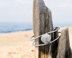 cast silver bay scallop shell cuff laying on driftwood by hkm jewelry hali maclaren
